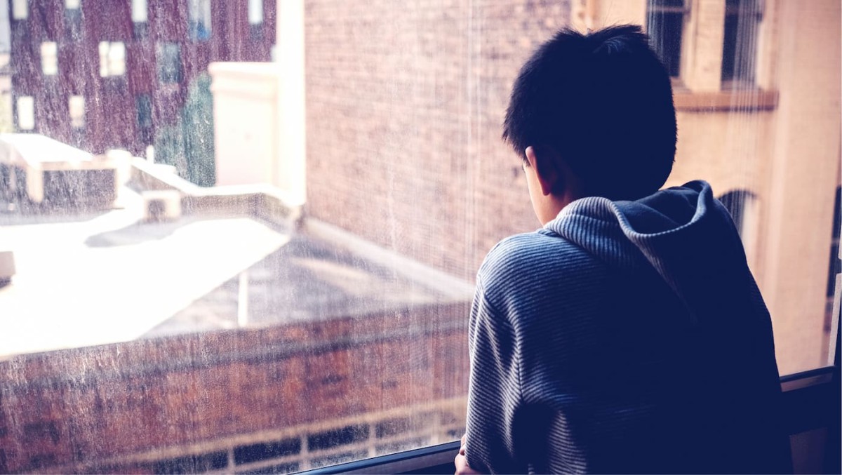 A child looking out of a window from a dark building