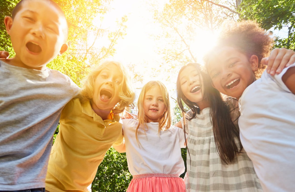 Group of five children smiling together in front of trees outdoors