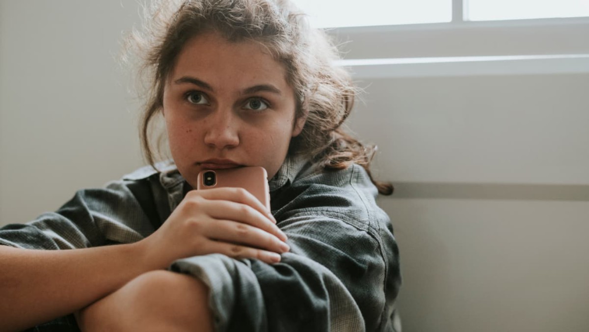 A young woman sitting on the floor near a window indoors with a troubled expression