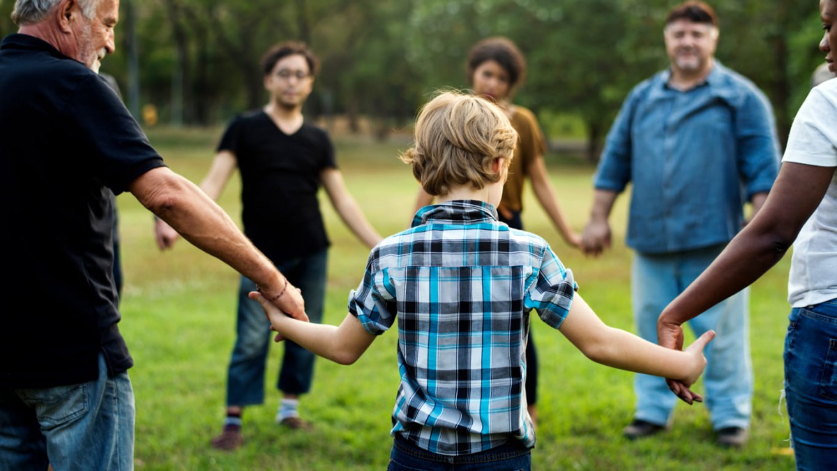 A large group of people of various ages holding hands in a circle outdoors