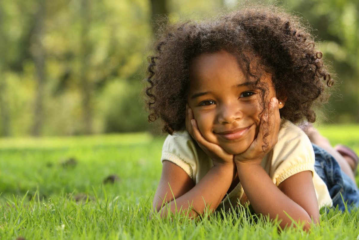 A child lying on her stomach in the grass and smiling