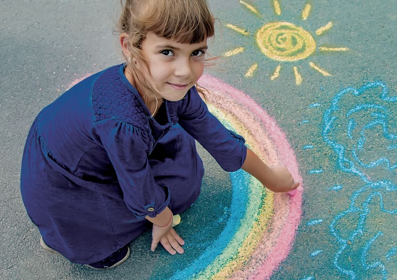 A child drawing a rainbow with chalk and smiling