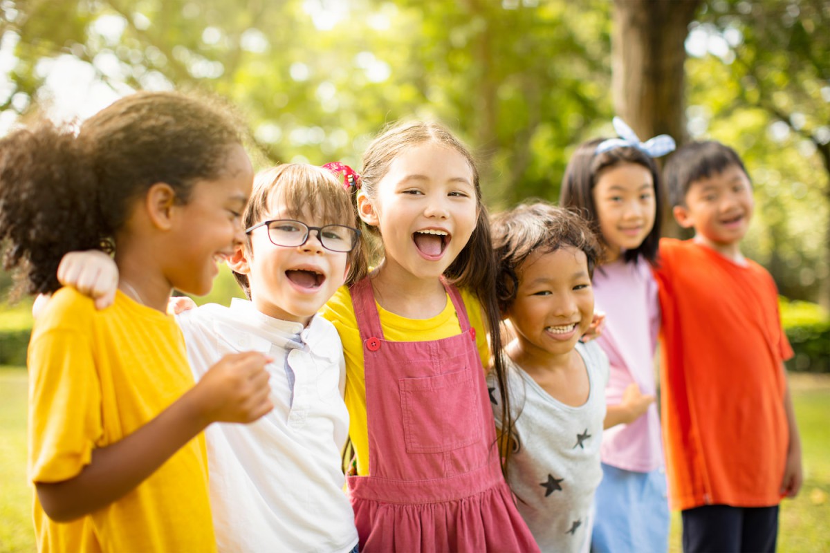 A group of six children holding hands smiling and laughing outdoors