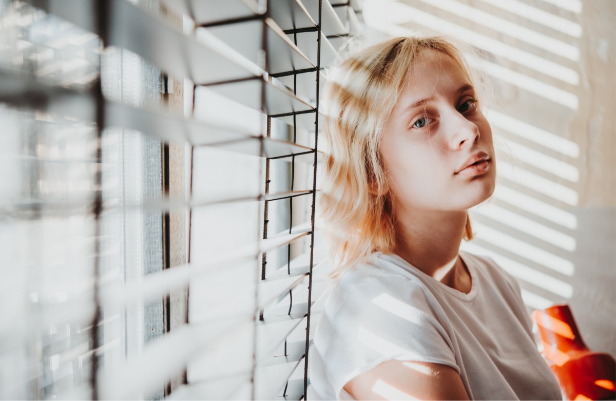 A girl leaning next to a window looking longingly at the camera