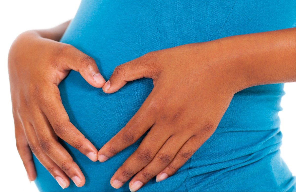 A pregnant woman with her hands over her belly making a heart shape