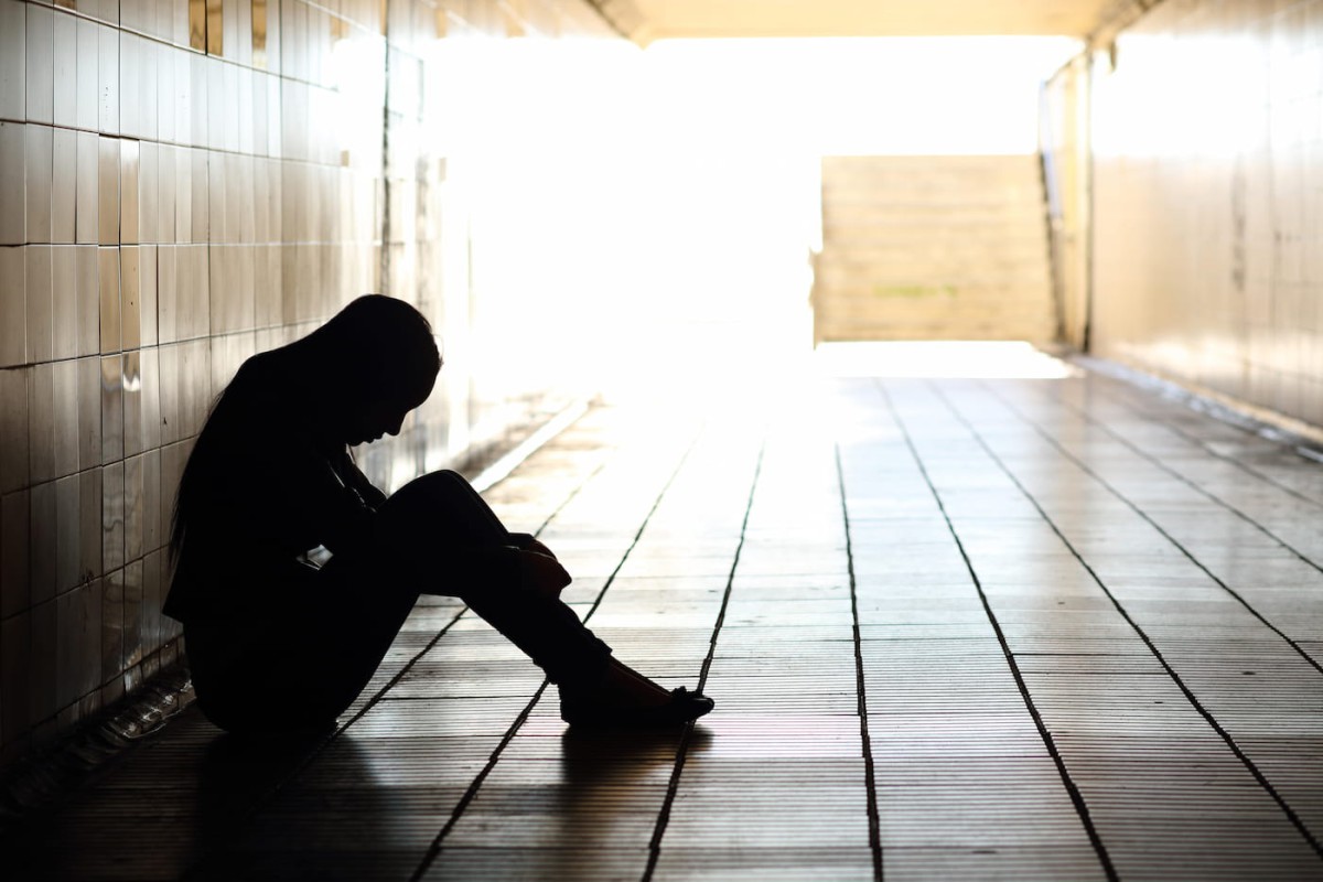 Silhouette of a teenager sitting on the floor in a dark hallway
