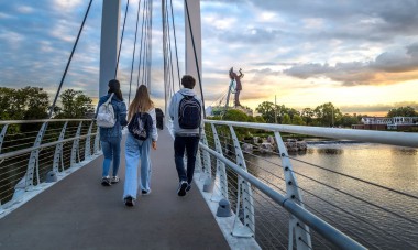 Young people walking on a bridge toward the Keeper of the Plains in Wichita, KS