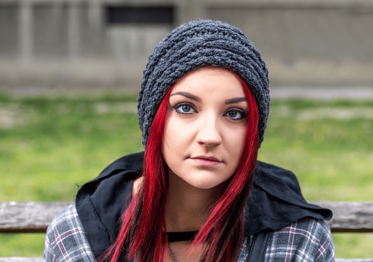 Teenage girl with red hair sitting on a park bench with a neutral expression