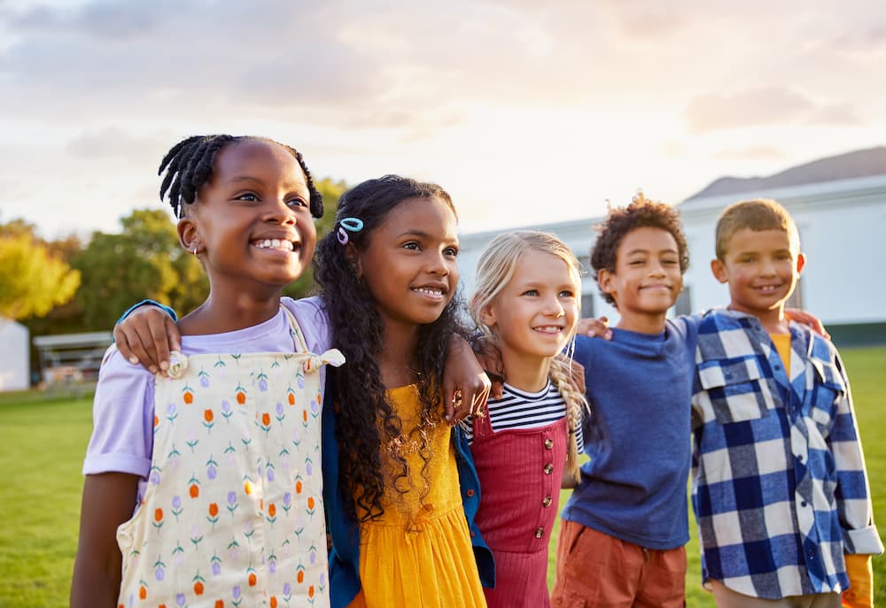 A group of five children smiling with their arms around each other