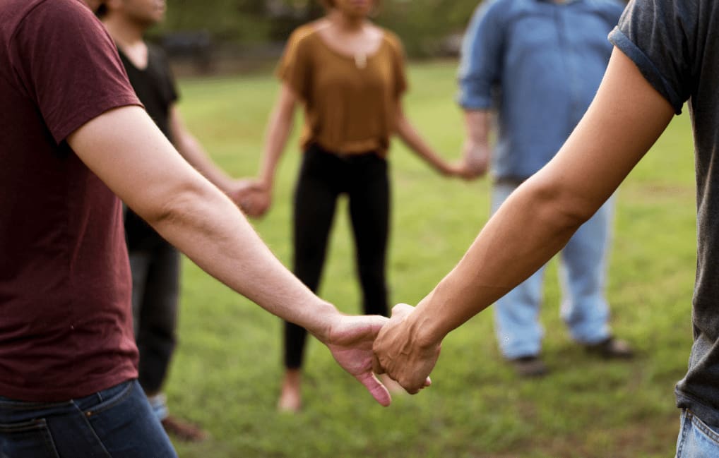 A group of people holding hands in a circle outdoors