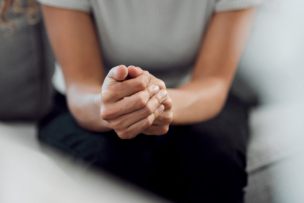 A person sitting with their hands folded in front of them