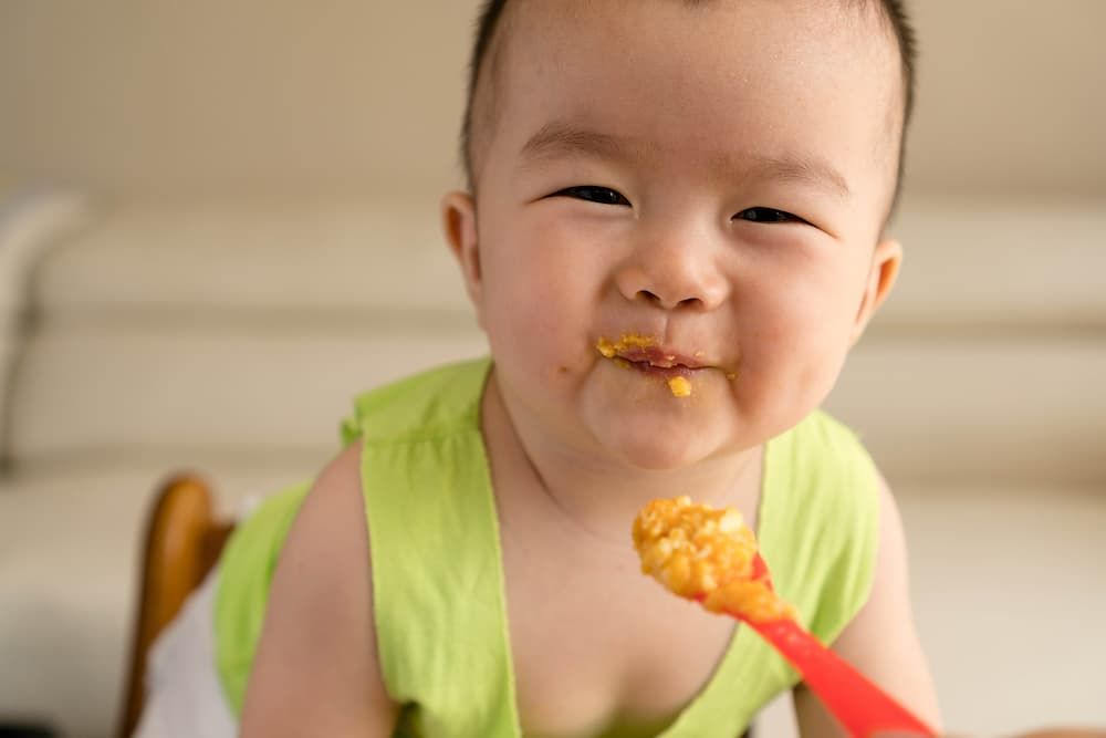 A happy baby eating baby food.
