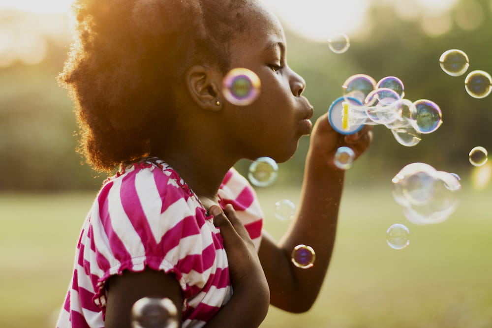 A young girl blowing bubbles outside