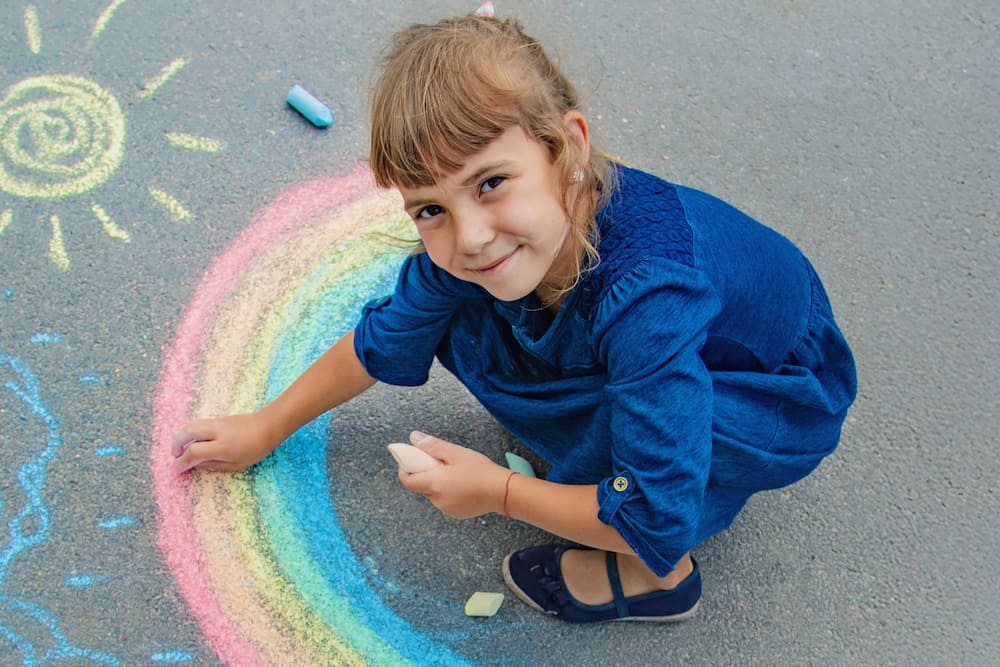 A young child drawing a rainbow with chalk