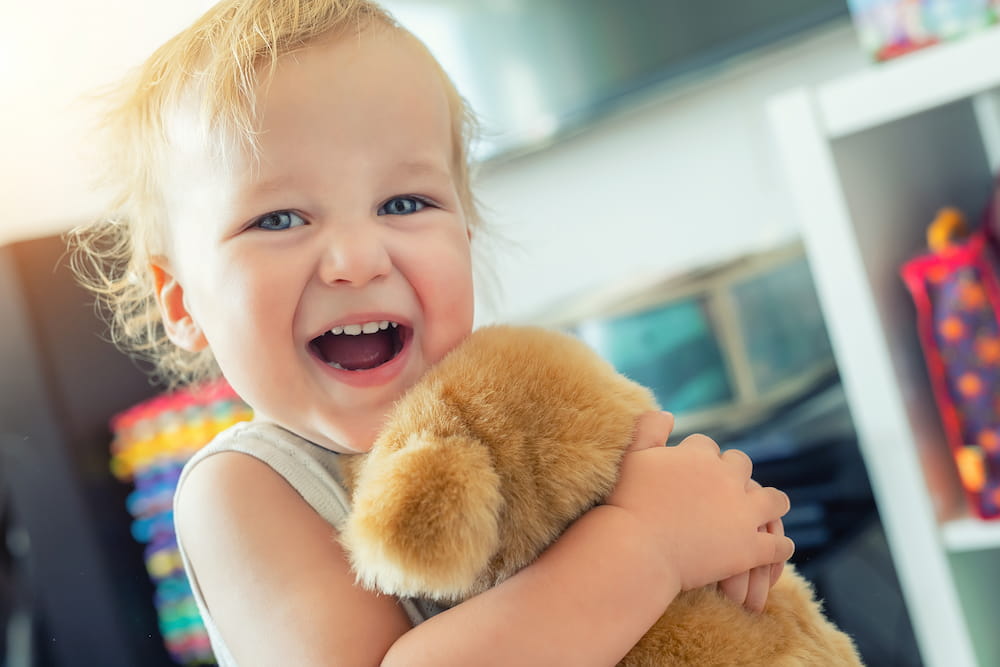 A toddler hugging a plushie and smiling