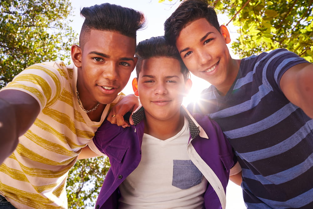 Three teenagers with their arms around one another's shoulders smiling at the camera
