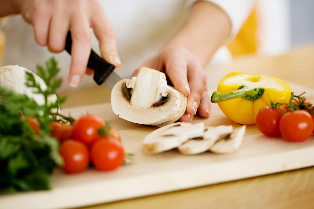 A person slicing a mushroom and fruits and vegetables
