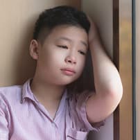 A young boy standing in a corner with a sad expression