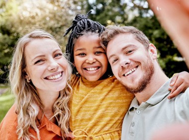 A child smiling with her foster parents at a park