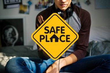 Teenager sitting on his bed with a Safe Place program sign