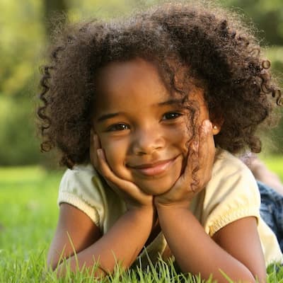 A child lying in the grass smiling at the camera